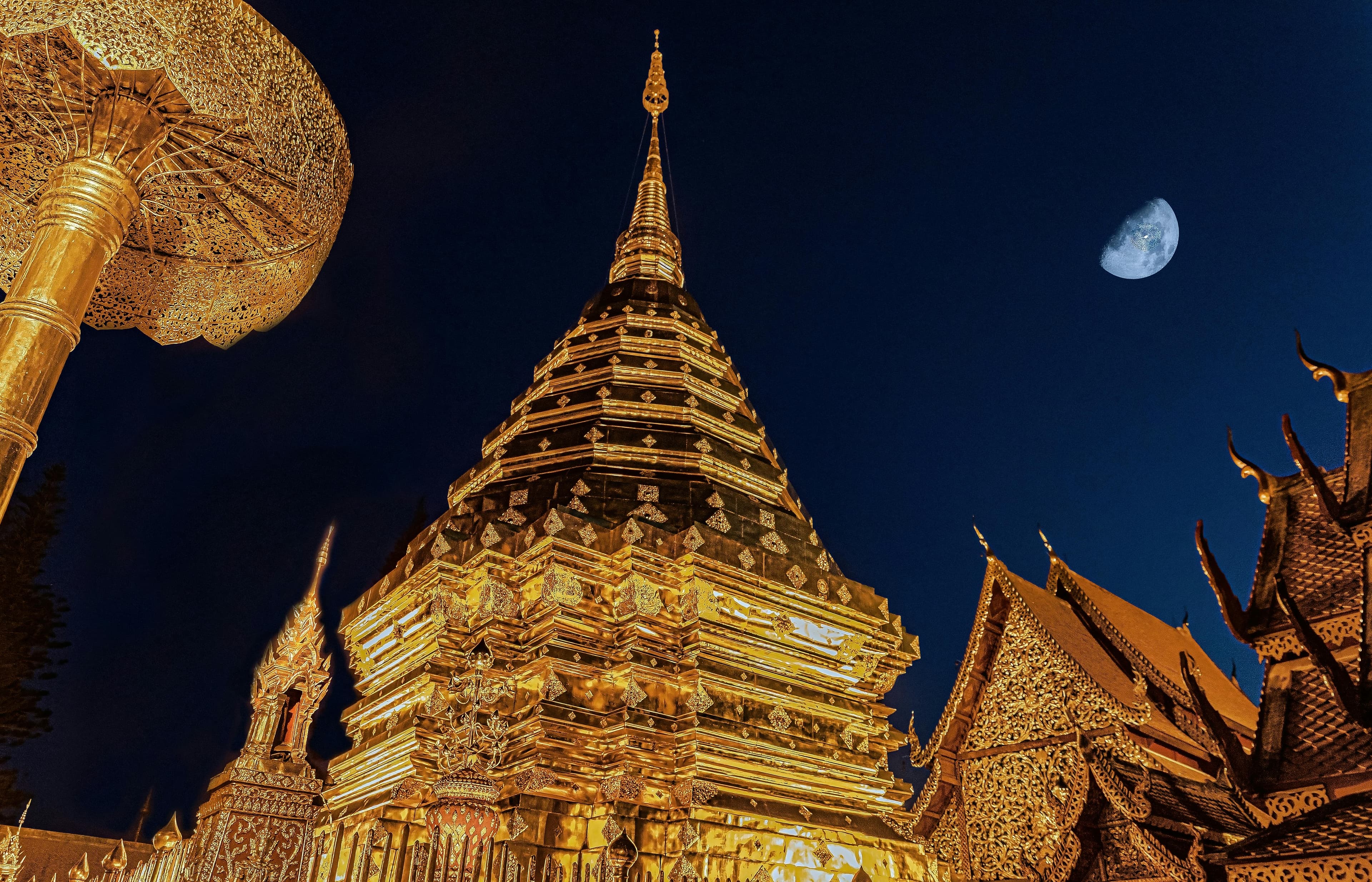 Doi Suthep golden chedi illuminated at night with the moon above Chiang Mai
