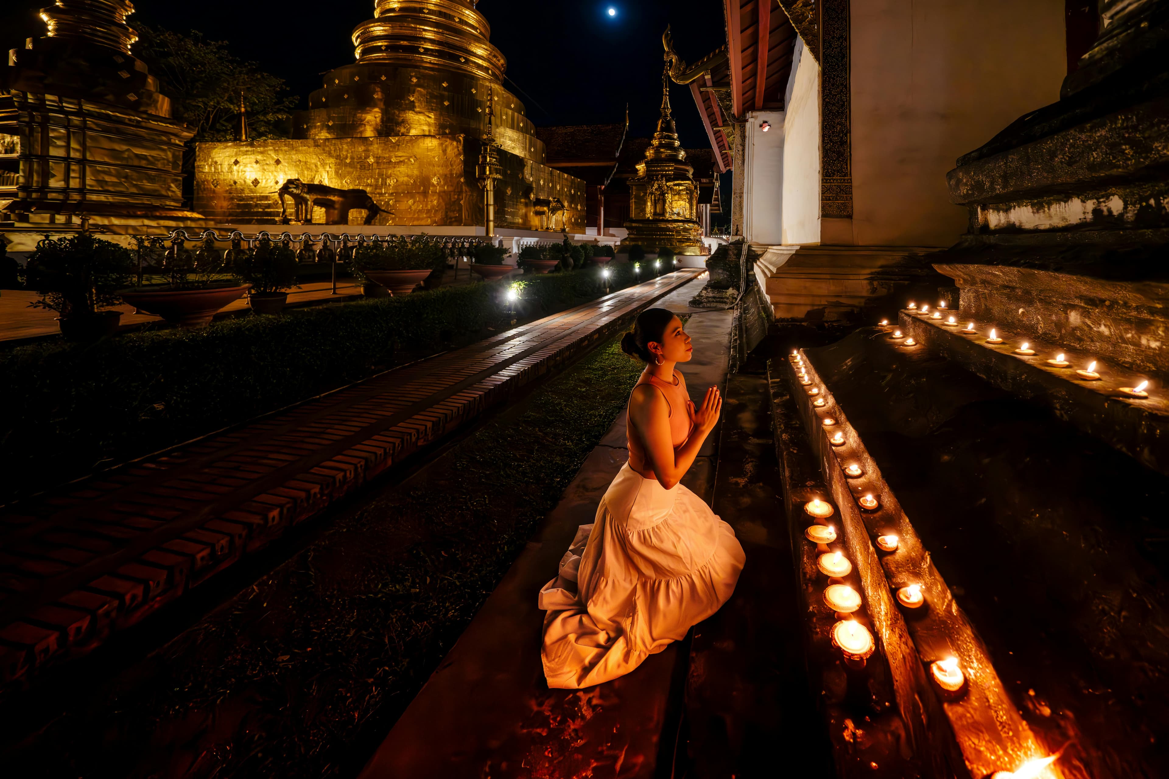 Woman praying by candlelight at a golden Buddhist temple in Chiang Mai at night