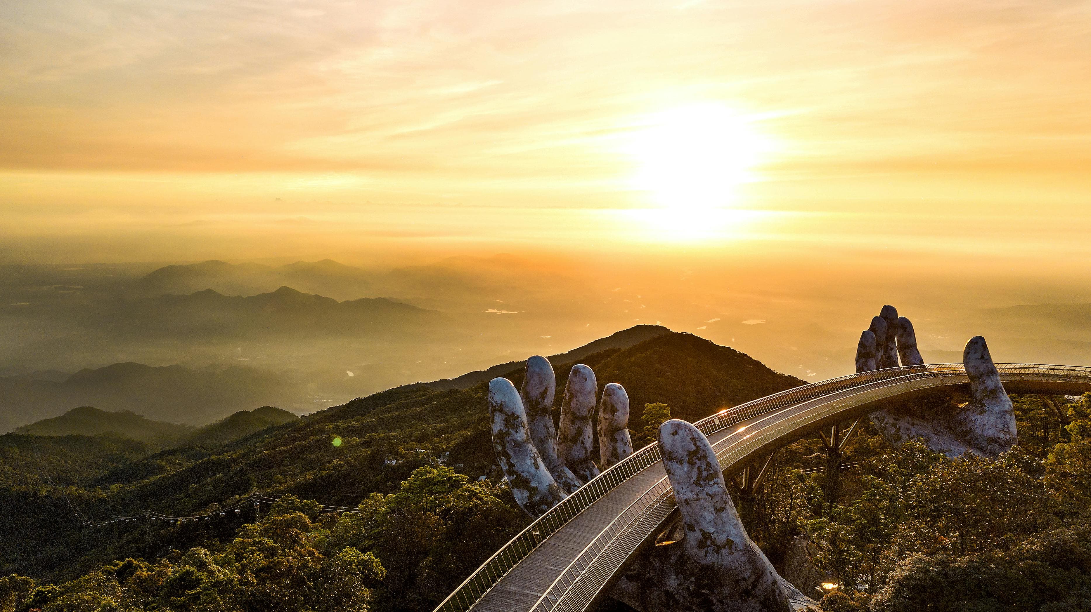 Aerial view of the Golden Bridge held by giant stone hands at Ba Na Hills Da Nang Vietnam at sunset