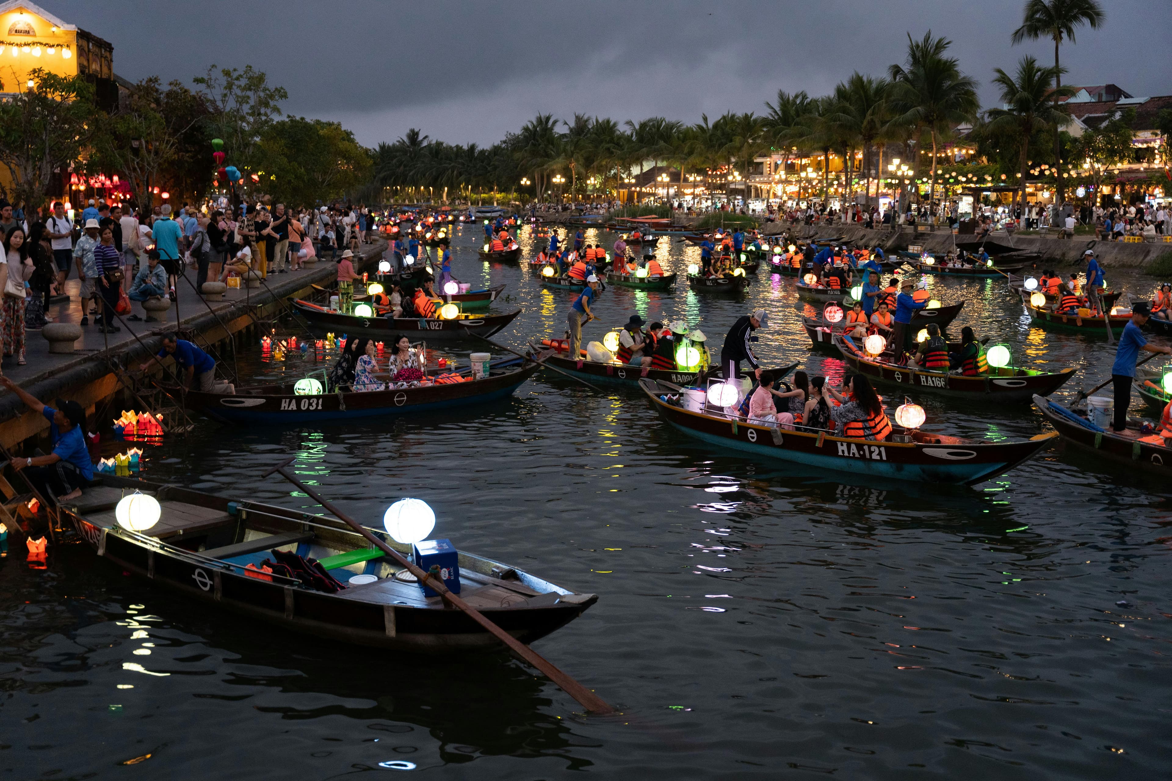Traditional wooden boats on Thu Bon River with lanterns glowing in Hoi An Old Town at sunset