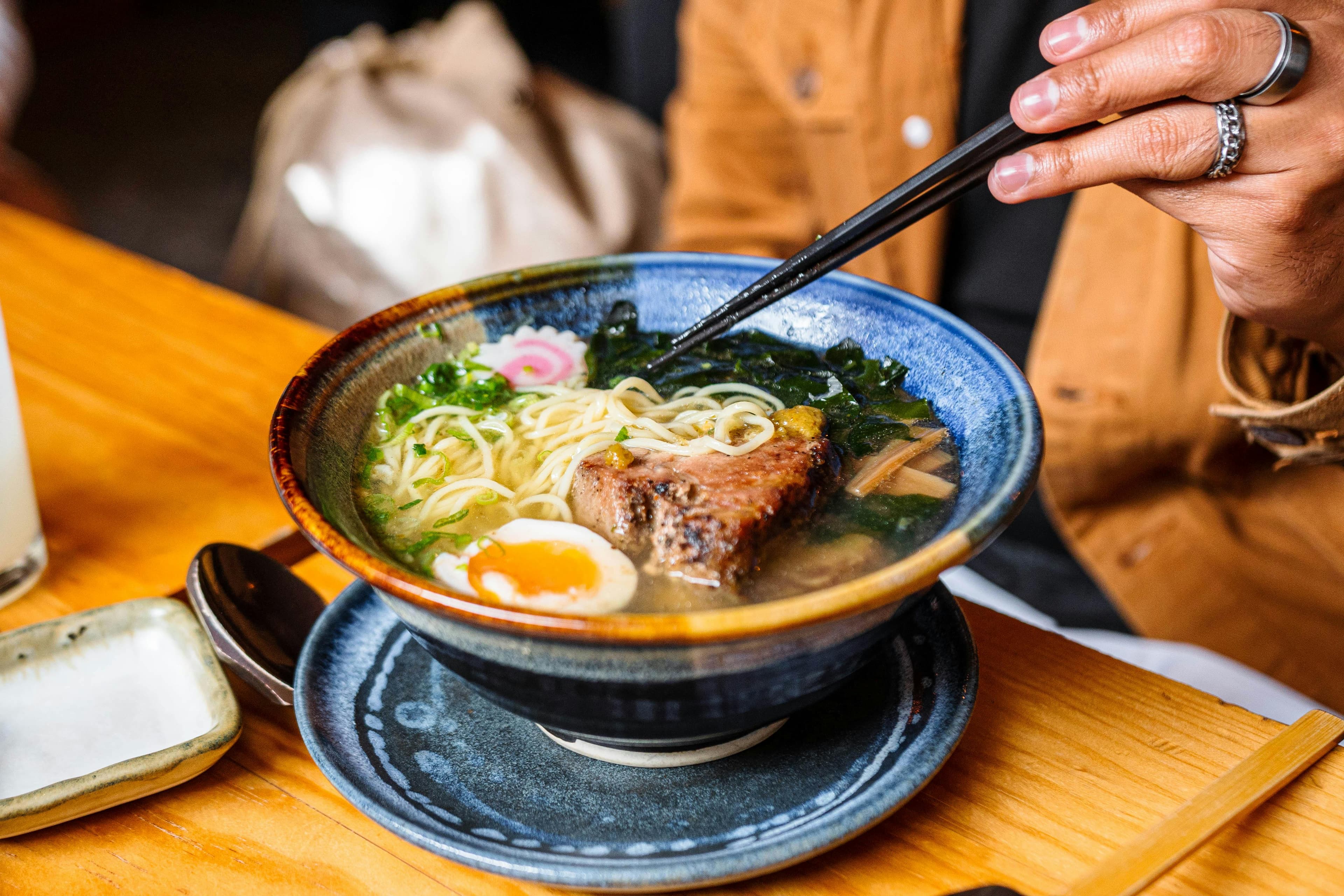 Bowl of tonkotsu ramen with chashu pork, soft-boiled egg, seaweed and scallions held with chopsticks