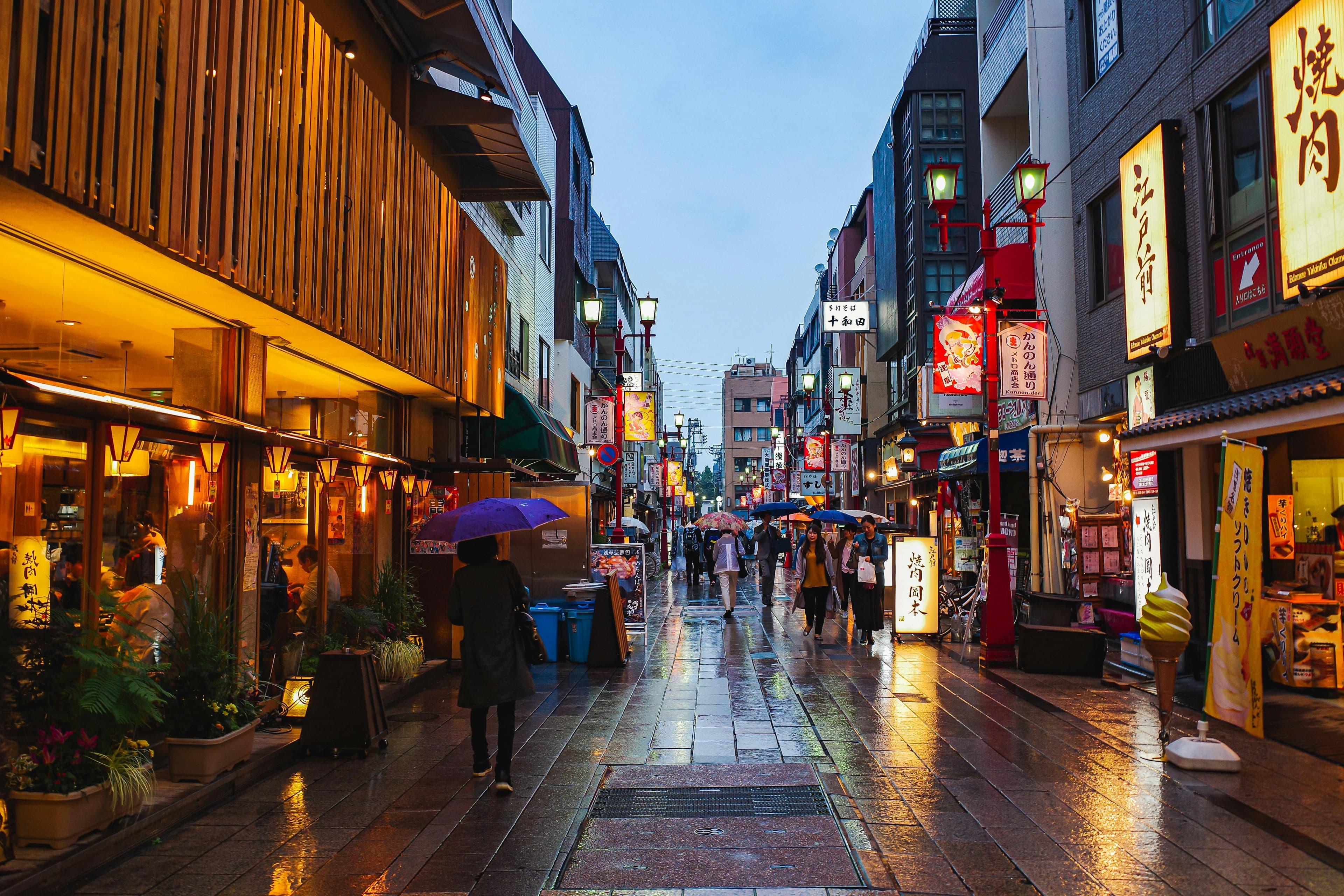 Traditional Tokyo street at dusk with red lanterns wet pavement and umbrellas in Yanaka Asakusa atmosphere